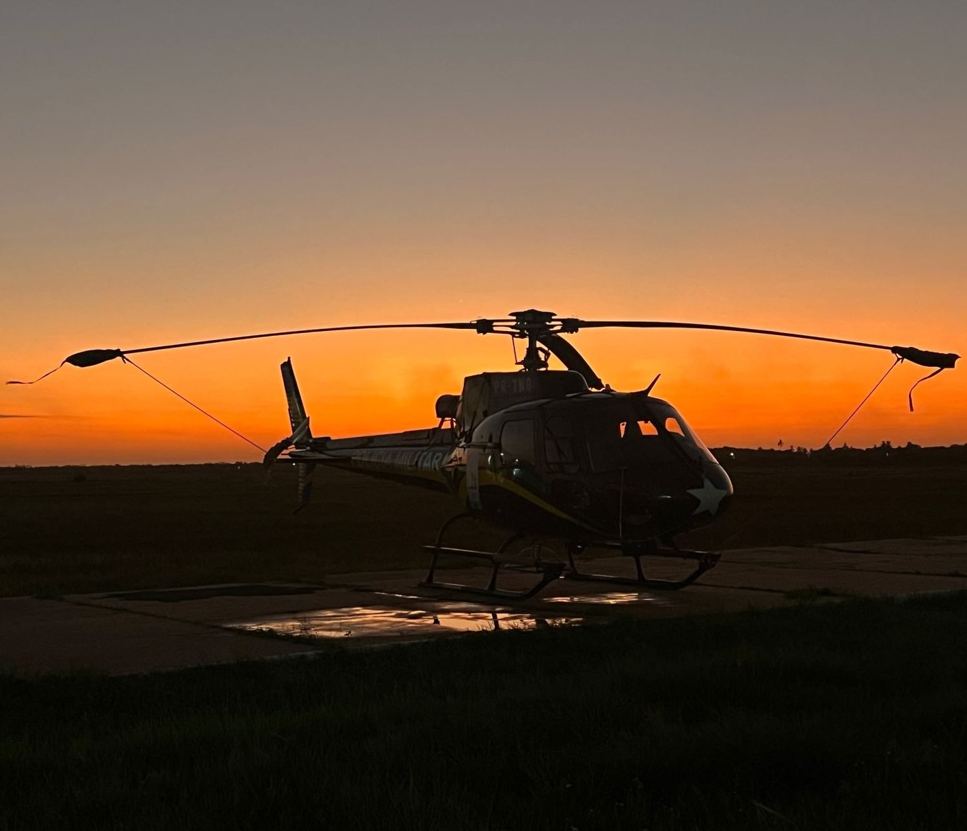 Helicóptero estacionado em silhueta diante de um pôr do sol alaranjado